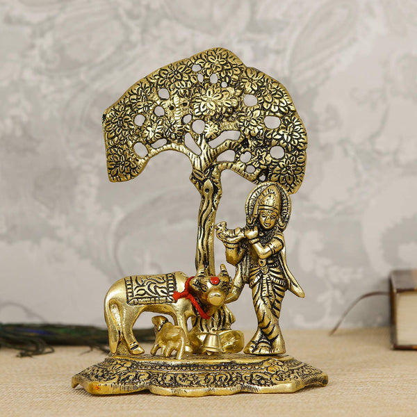 Intricate Lord Krishna showpiece in metal, depicting the deity playing the flute under a tree, surrounded by a golden cow and calf.