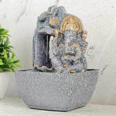 A water fountain featuring a statue of Lord Ganesha, the Hindu god of wisdom and remover of obstacles. Water flows around or from the statue, creating a serene and calming atmosphere. The fountain may be made of stone, marble, or other materials and may have additional decorative elements, such as plants or lights