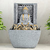 A water fountain featuring a statue of Lord Buddha, the founder of Buddhism, surrounded by cascading waterfalls or a serene pool of water. The fountain may be made of stone, marble, or other materials and may have additional decorative elements, such as plants or lights.