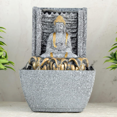A water fountain featuring a statue of Lord Buddha, the founder of Buddhism, surrounded by cascading waterfalls or a serene pool of water. The fountain may be made of stone, marble, or other materials and may have additional decorative elements, such as plants or lights.