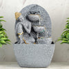 A water fountain featuring a statue of Lord Buddha, the founder of Buddhism, surrounded by cascading waterfalls or a serene pool of water. The fountain may be made of stone, marble, or other materials and may have additional decorative elements, such as plants or lights.
