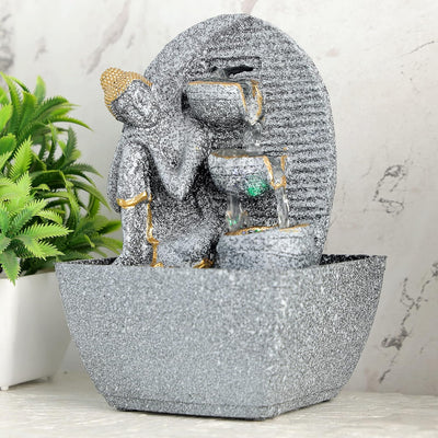 A water fountain featuring a statue of Lord Buddha, the founder of Buddhism, surrounded by cascading waterfalls or a serene pool of water. The fountain may be made of stone, marble, or other materials and may have additional decorative elements, such as plants or lights.