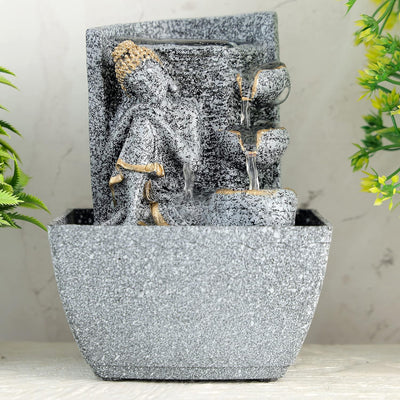 A water fountain featuring a statue of Lord Buddha, the founder of Buddhism, surrounded by cascading waterfalls and lush greenery. The fountain may be made of stone, marble, or other materials and may have additional decorative elements.