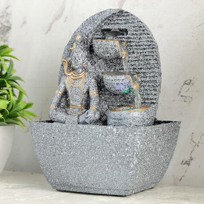 A small, tabletop fountain made of polyresin, a durable and lightweight material. Water flows through the fountain, creating a soothing sound. The fountain may have additional decorative elements, such as rocks, plants, or a figurine.