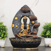 A Hindu-inspired water fountain featuring statues of various Hindu gods, including Buddha, surrounded by cascading waterfalls and lush greenery. The fountain is likely made of stone or marble and has a traditional Indian design.