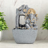 A water fountain featuring a statue of Lord Ganesha, the Hindu god of wisdom and remover of obstacles. Water flows around or from the statue, creating a serene and calming atmosphere. The fountain may be made of stone, marble, or other materials and may have additional decorative elements, such as plants or lights