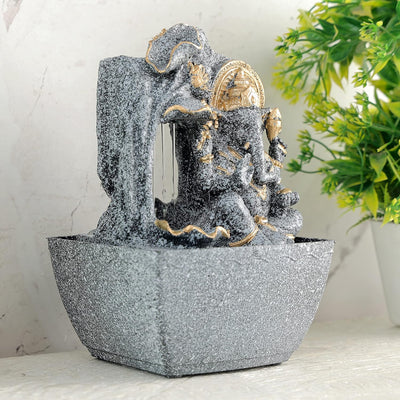 A water fountain featuring a statue of Lord Ganesha, the Hindu god of wisdom and remover of obstacles. Water flows around or from the statue, creating a serene and calming atmosphere. The fountain may be made of stone, marble, or other materials and may have additional decorative elements, such as plants or lights