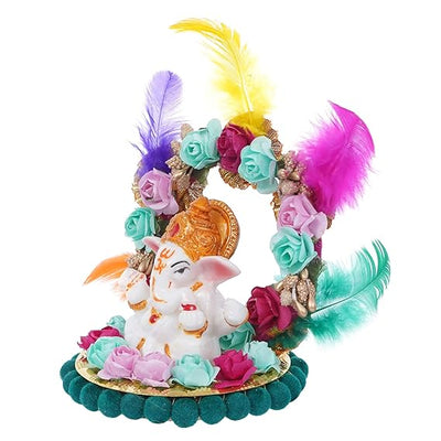 A small golden idol of Lord Ganesha, the Hindu god of wisdom and remover of obstacles, seated on a throne made of colorful flowers. The idol is placed on a car dashboard.