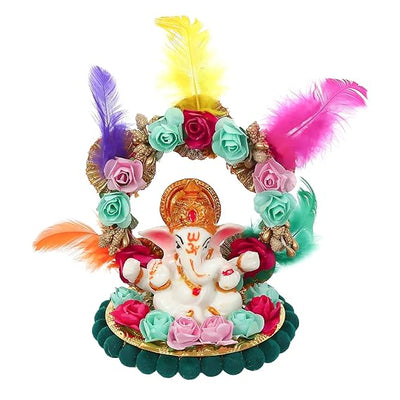 A small golden idol of Lord Ganesha, the Hindu god of wisdom and remover of obstacles, seated on a throne made of colorful flowers. The idol is placed on a car dashboard.
