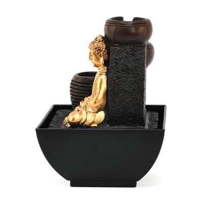 A water fountain featuring a statue of Buddha seated in meditation pose. Water flows from the Buddha's hands or from a nearby source, creating a serene and calming atmosphere. The fountain may be made of stone, marble, or other materials and may have additional decorative elements.