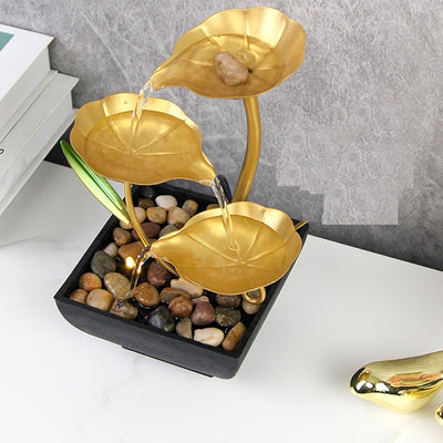 A small, tabletop fountain made of metal. Water flows through the metal pipes or channels, creating a soothing sound. The fountain may have additional decorative elements, such as rocks, plants, or a figurine.