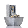 A water fountain featuring a statue of Lord Buddha, the founder of Buddhism, surrounded by cascading waterfalls or a serene pool of water. The fountain may be made of stone, marble, or other materials and may have additional decorative elements, such as plants or lights.