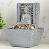 A water fountain featuring a statue of Lord Buddha, the founder of Buddhism, surrounded by cascading waterfalls or a serene pool of water. The fountain may be made of stone, marble, or other materials and may have additional decorative elements, such as plants or lights.