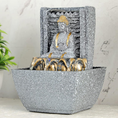 A water fountain featuring a statue of Lord Buddha, the founder of Buddhism, surrounded by cascading waterfalls or a serene pool of water. The fountain may be made of stone, marble, or other materials and may have additional decorative elements, such as plants or lights.