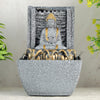 A water fountain featuring a statue of Lord Buddha, the founder of Buddhism, surrounded by cascading waterfalls or a serene pool of water. The fountain may be made of stone, marble, or other materials and may have additional decorative elements, such as plants or lights.