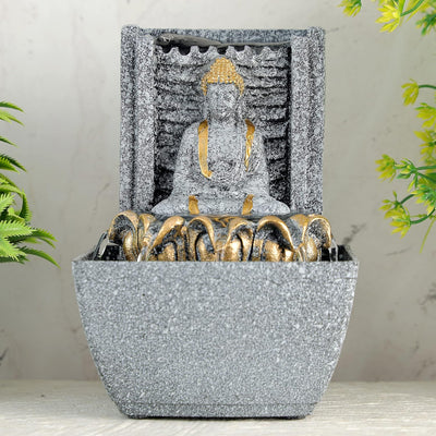A water fountain featuring a statue of Lord Buddha, the founder of Buddhism, surrounded by cascading waterfalls or a serene pool of water. The fountain may be made of stone, marble, or other materials and may have additional decorative elements, such as plants or lights.