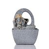 A small, tabletop fountain featuring a statue of Lord Ganesha, the Hindu god of wisdom and remover of obstacles. Water flows around or from the statue, creating a serene and calming atmosphere. The fountain may be made of stone, marble, or other materials and may have additional decorative elements, such as plants or lights