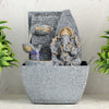A small, tabletop fountain made of polyresin, a durable and lightweight material, featuring a statue of Lord Ganesha, the Hindu god of wisdom and remover of obstacles. Water flows around or from the statue, creating a serene and calming atmosphere. The fountain may have additional decorative elements, such as plants or lights.