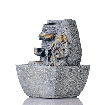 A small, tabletop fountain made of polyresin, a durable and lightweight material, featuring a statue of Lord Ganesha, the Hindu god of wisdom and remover of obstacles. Water flows around or from the statue, creating a serene and calming atmosphere. The fountain may have additional decorative elements, such as plants or lights.