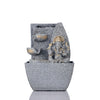 A small, tabletop fountain made of polyresin, a durable and lightweight material, featuring a statue of Lord Ganesha, the Hindu god of wisdom and remover of obstacles. Water flows around or from the statue, creating a serene and calming atmosphere. The fountain may have additional decorative elements, such as plants or lights.