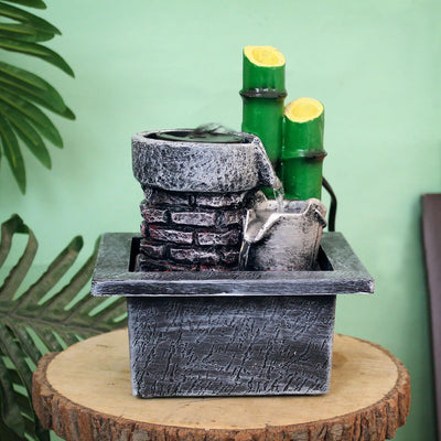 A small, tabletop water fountain made of bamboo. Water flows through the bamboo pipes, creating a soothing sound. The fountain may have additional decorative elements, such as rocks or plants.