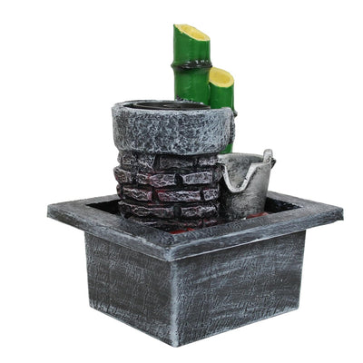 A small, tabletop water fountain made of bamboo. Water flows through the bamboo pipes, creating a soothing sound. The fountain may have additional decorative elements, such as rocks or plants.
