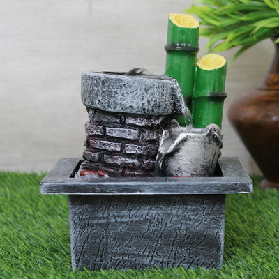 A small, tabletop water fountain made of bamboo. Water flows through the bamboo pipes, creating a soothing sound. The fountain may have additional decorative elements, such as rocks or plants.